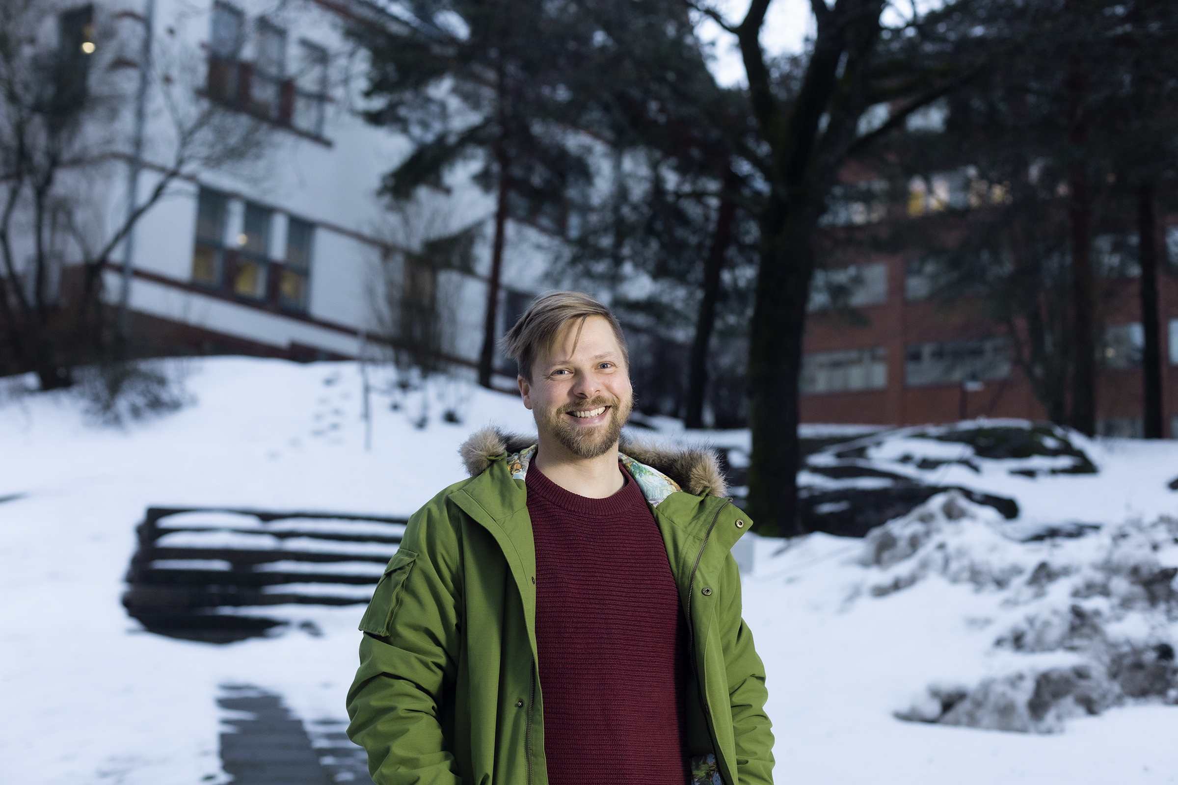 Tomi seisoo ulkona ja katsoo kameraan. Takana näkyy puita ja kerrostaloa.